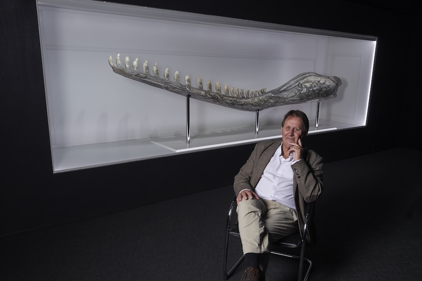 A man sits in front of engraved four-metre sperm whale jaw bone