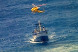 A yellow helicopter hovering above a small fishing boat in the middle of the ocean