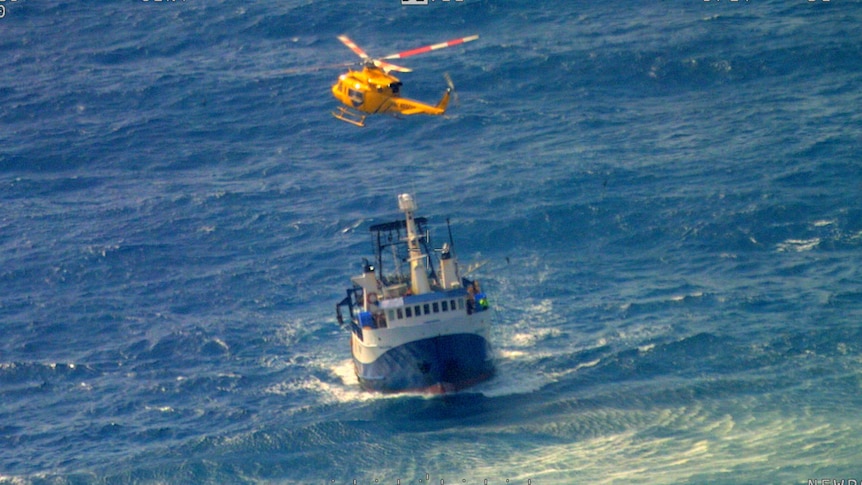 A yellow helicopter hovering above a small fishing boat in the middle of the ocean