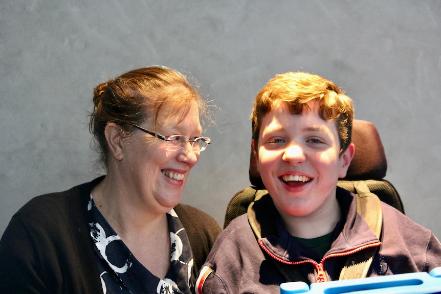 A woman with brown hair looking at her son, both of whom are smiling