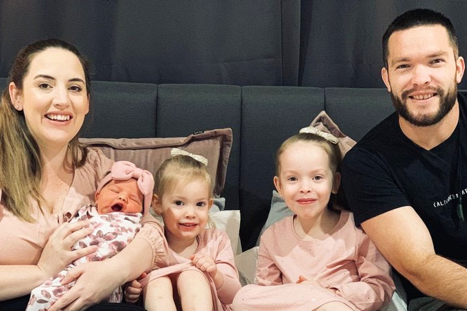 Chloe Aitken, with her three children and partner, sit on a couch.