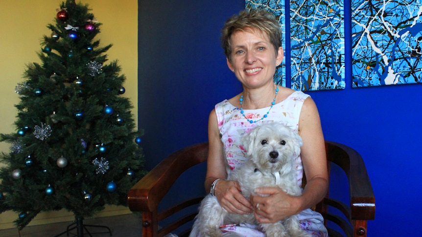 Deb Rae sitting inside her Mackay home with her dog called Jingles and the Christmas tree