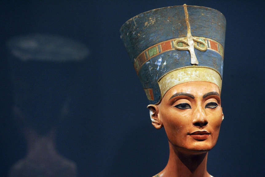 A limestone figure of a woman with a long elegant neck and a sharp jawline. She is wearing eyeliner around her eyes.