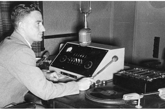Man sitting at old circa 1950's news desk with mic playing the new chime on a xylophone.