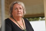 A close up photo of an older woman standing on her porch looking at the sky.