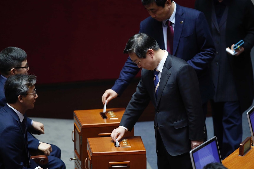 Politicians place their votes in a ballot box.