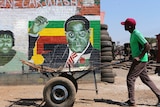 A man pushes an empty cart on a dirt road past a street art portrait of former Zimbabwean President Robert Mugabe.