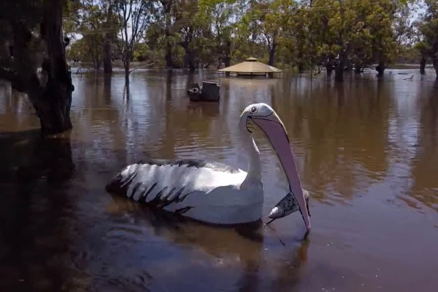 A large sculpture of a pelican eating a fish surrounded by water and trees