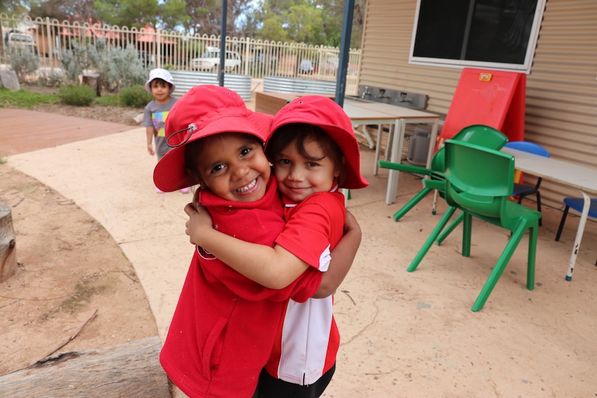 Koonibba Aboriginal School students hugging one another in their red school uniforms wearing hats. 