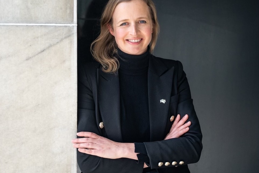 Emily Bourke, standing against a white and black wall with a big smile.