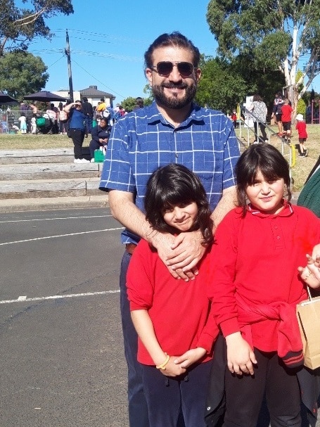 A man with beard and sunglasses and checked shirt with two girls in red t-shirts