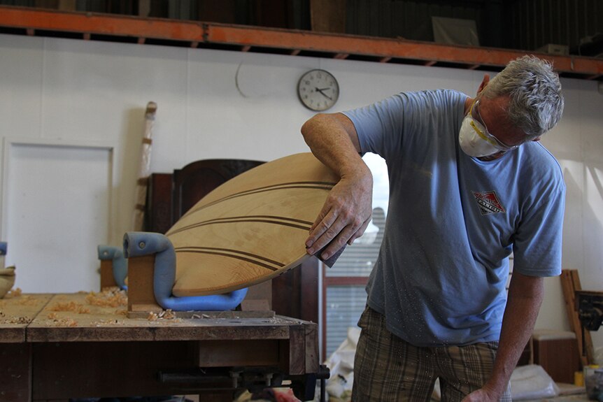 A man sanding a surfboard in a woodworking shop.