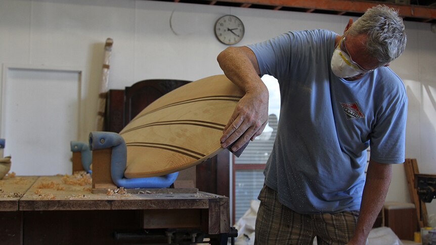 A man sanding a surfboard in a woodworking shop.