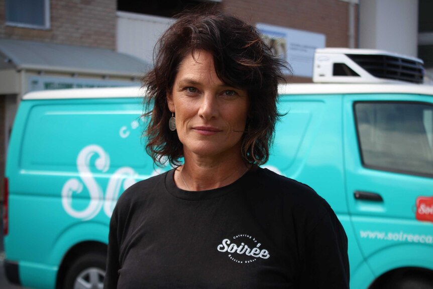 A woman in a black shirt stands in front of a blue van