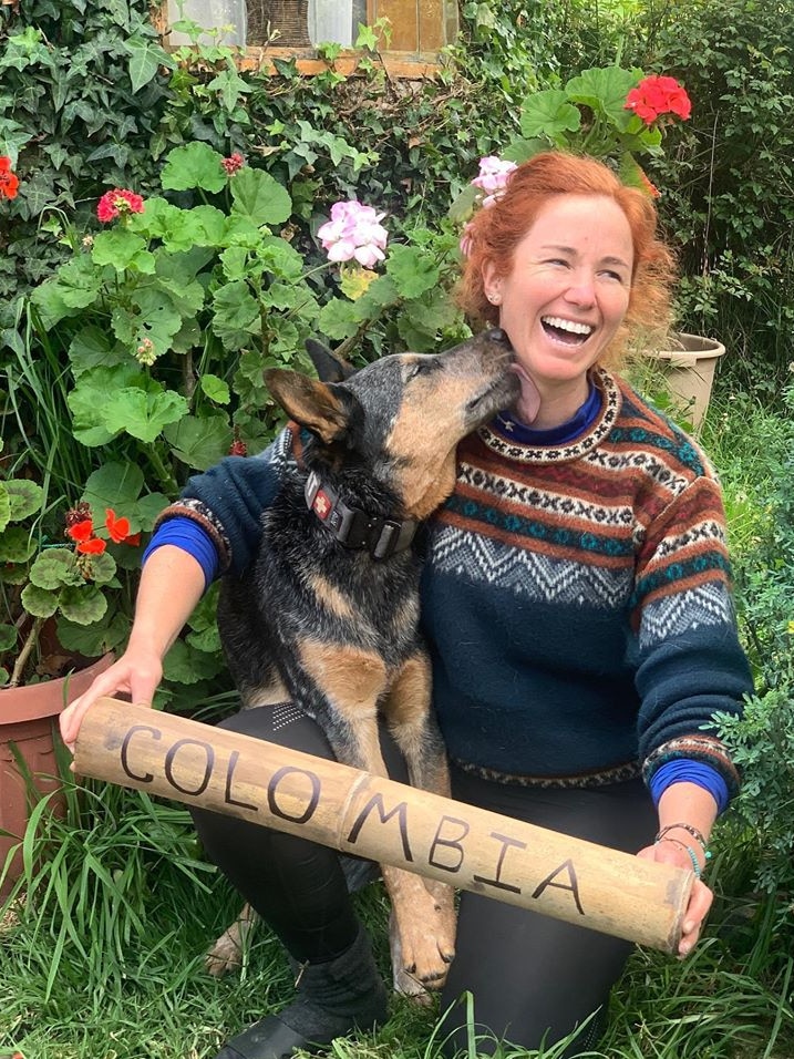 Lucy Barnard kneeling holding Colombia sign looking away from lens laughing as dog Wombat licks neck