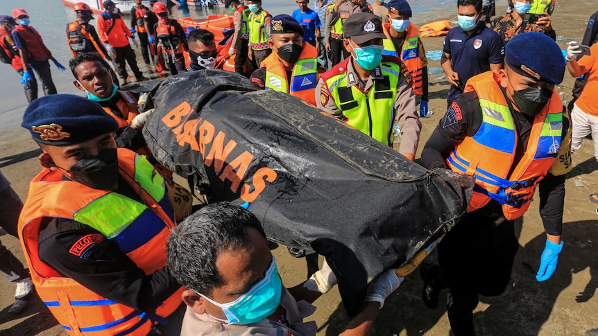 rescue team carry a body bag from the sea.