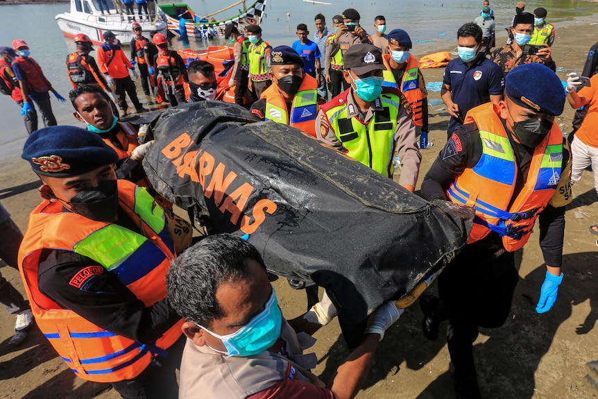rescue team carry a body bag from the sea.