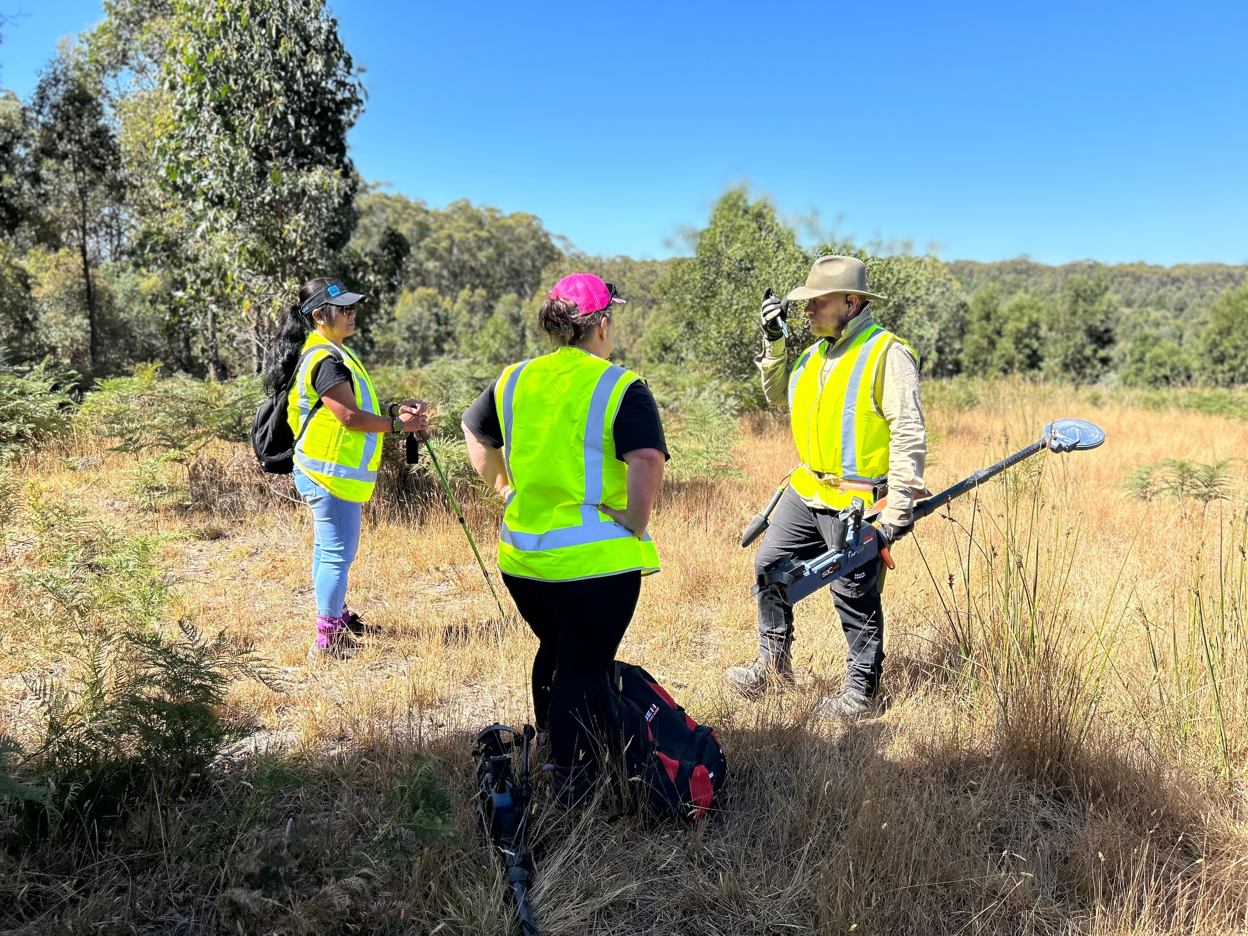 Three people in high-vis vests stand in bushland.