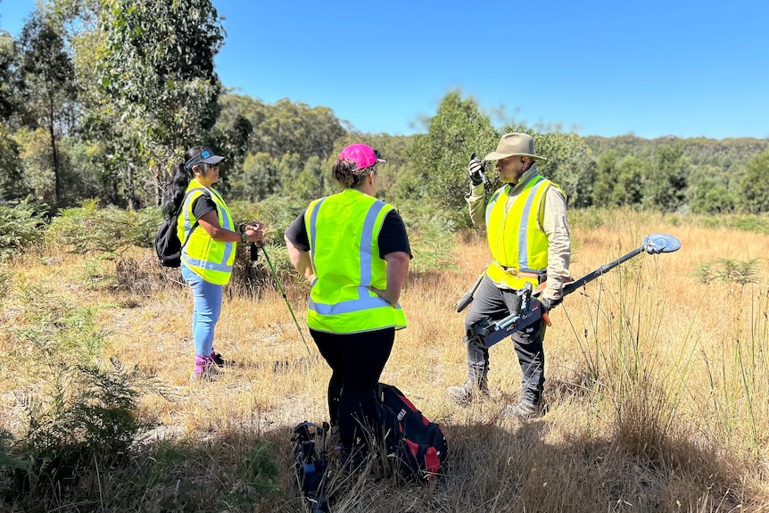 Three people in high-vis vests stand in bushland.