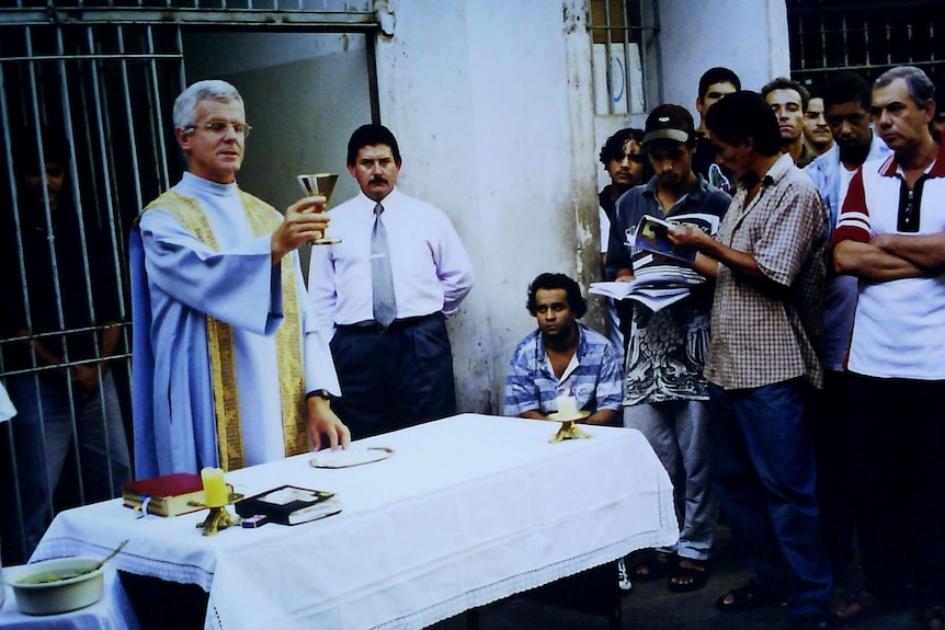 Father Mahony conducting service in Brazilian prison, lifting up communion cup.