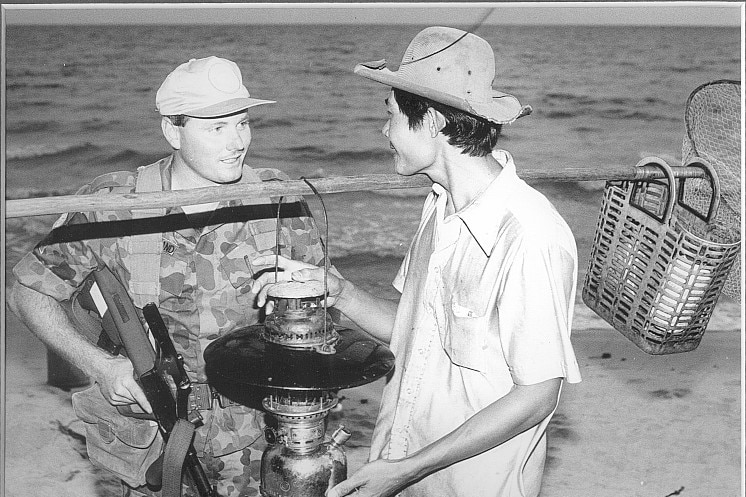 Paul Copeland with a machine gun, smiling as he chats with a Cambodian fisherman by the sea.
