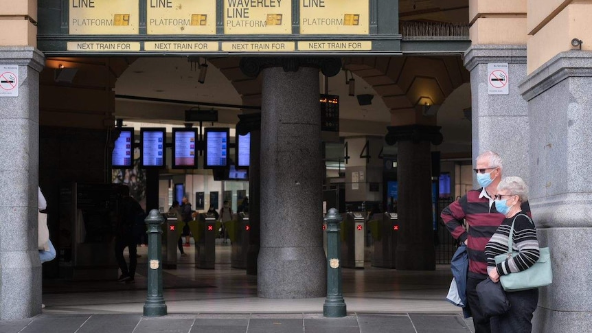 A couple in masks stand outside Flinders Street Station.