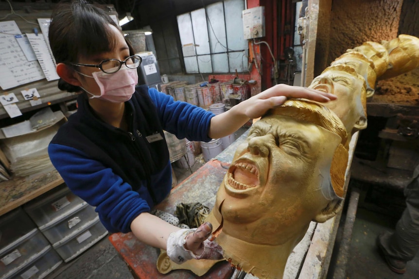 A worker wearing a face mask examines a rubber mask of Donald Trump.