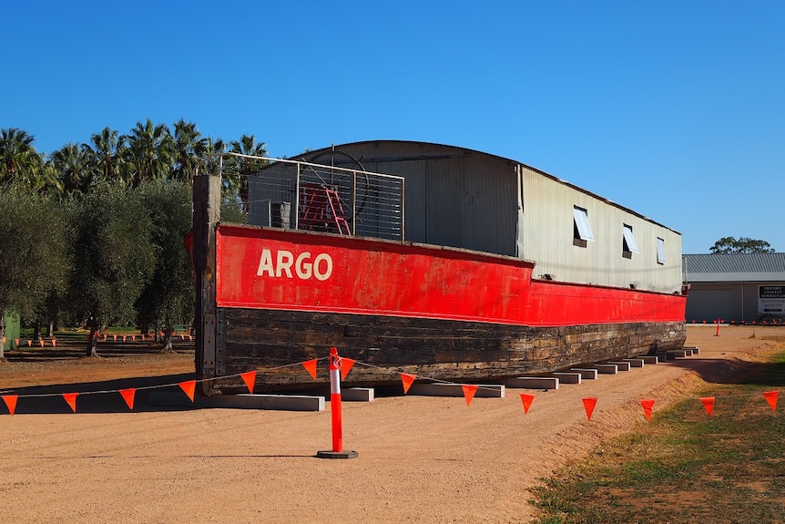 A salvaged barge sits as a static display on a patch of dirt outside a museum. It's very big