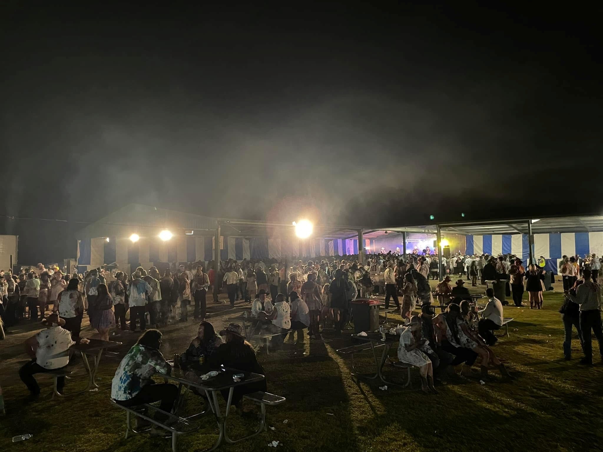 A crowd of people outside a tent wearing black tie clothing covered in food dye