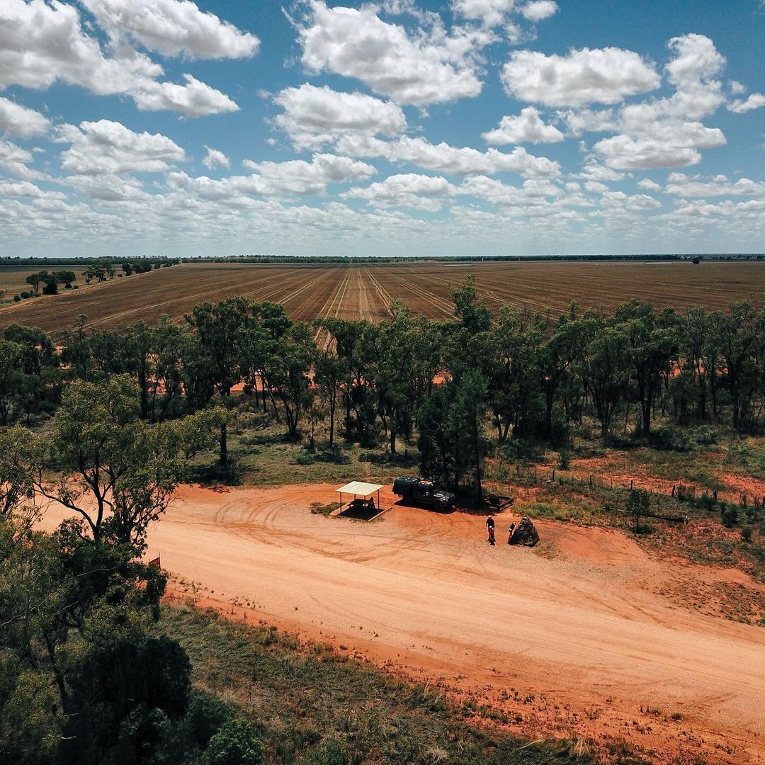 A dirt road with a shade shelter and a small stone mountain sculpture in front of a green pasture.