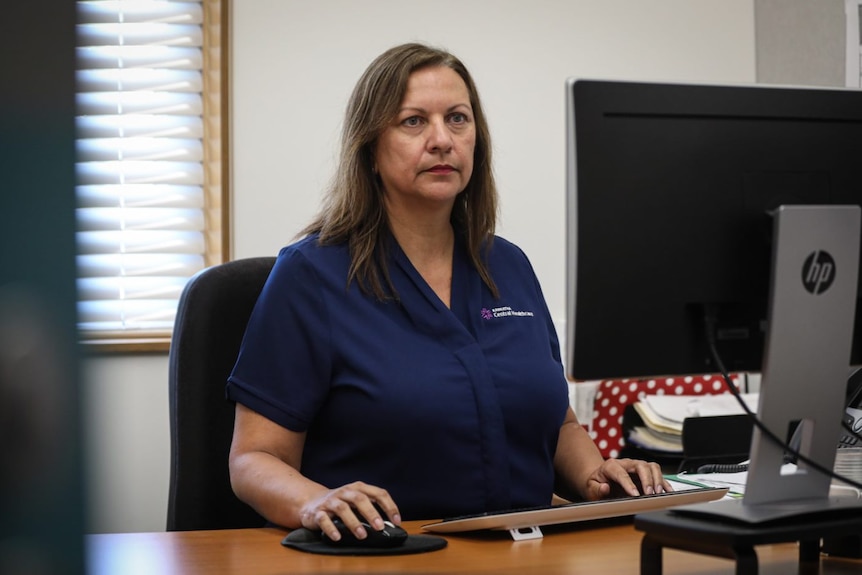 Dark haired woman in blue top sits at desk