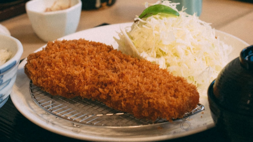 Crumbed pork on a plate with a pile of cabbage, and separate dishes at the front.