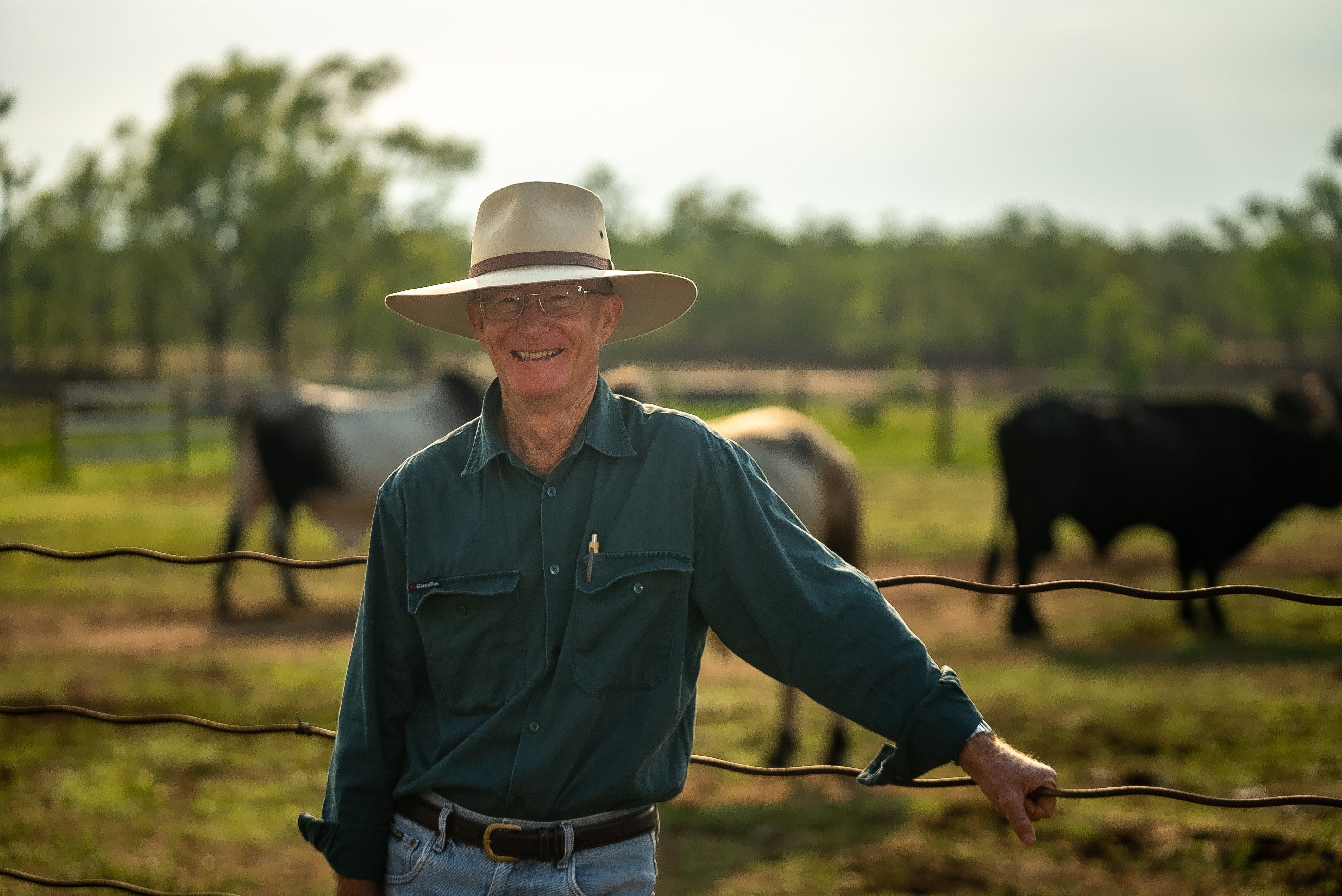 Un hombre sonríe frente a un ganado borroso a lo lejos.