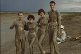 Four young people covered in mud posing for a photo next to a tidal flat.