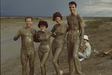 Four young people covered in mud posing for a photo next to a tidal flat.