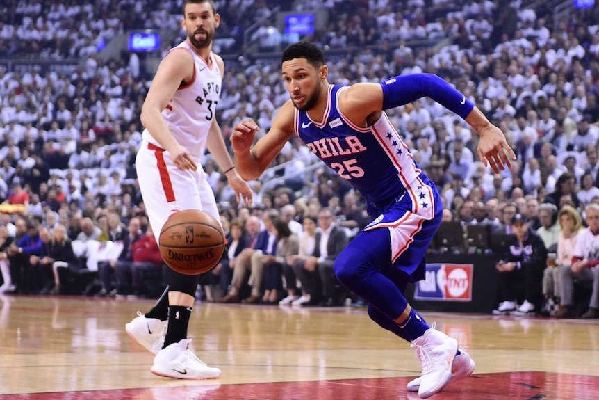 Ben Simmons runs after the ball while wearing a blue singlet as a man in a white singlet looks on