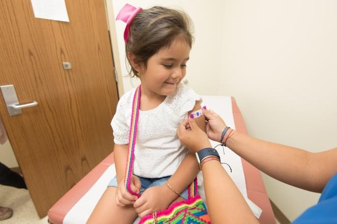 Health care provider places a bandage on the injection site of a child.