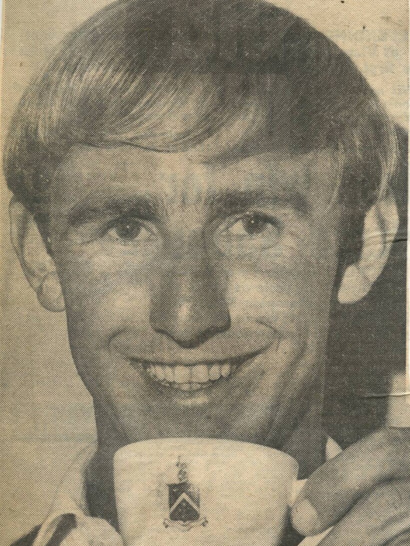 A black and white picture of a man with a cup of tea smiling