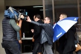 Katrina East arriving at Bunbury Court, hiding under an umbrella, while her father pushes away a camera man.