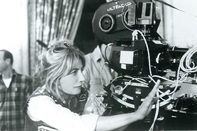 a woman holds her hand up to frame a shot with a movie camera behind her