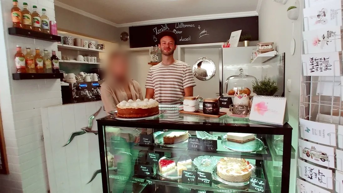 一名年轻男子和一名女子站在咖啡馆的蛋糕柜台后面。