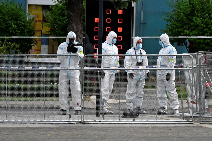Several people wearing haz-mat suits stand near a crime scene.