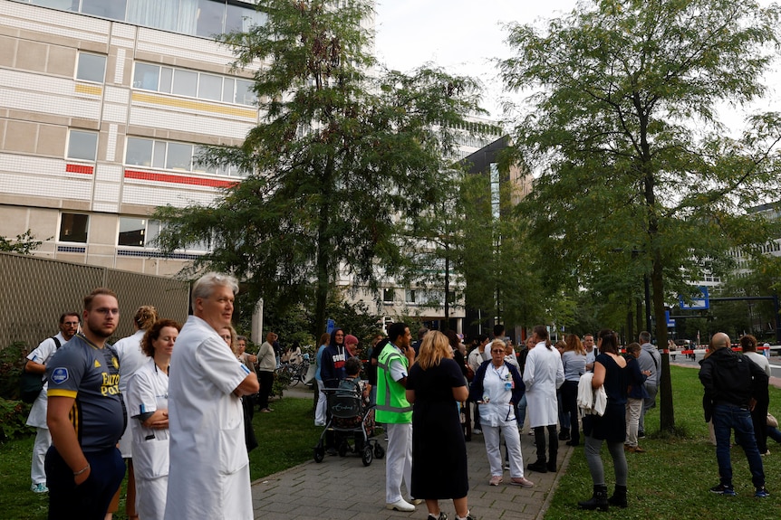 People are standing outside the hospital, some wearing white coats. 