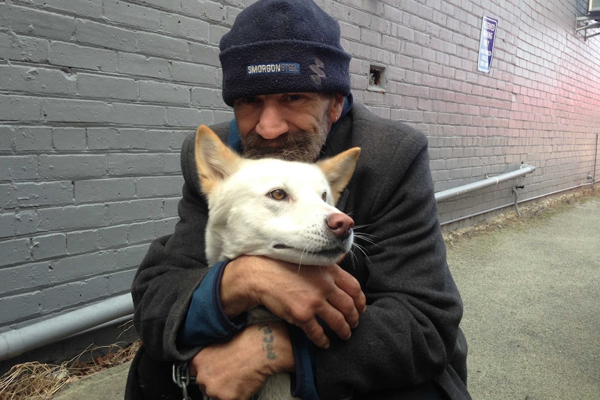 Homeless man hugs  pale coloured dog with golden ears.