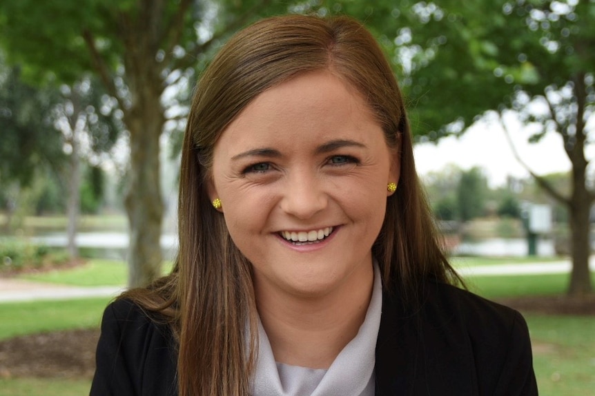 Jacqui Hawkins smiles while outdoors in front of trees.