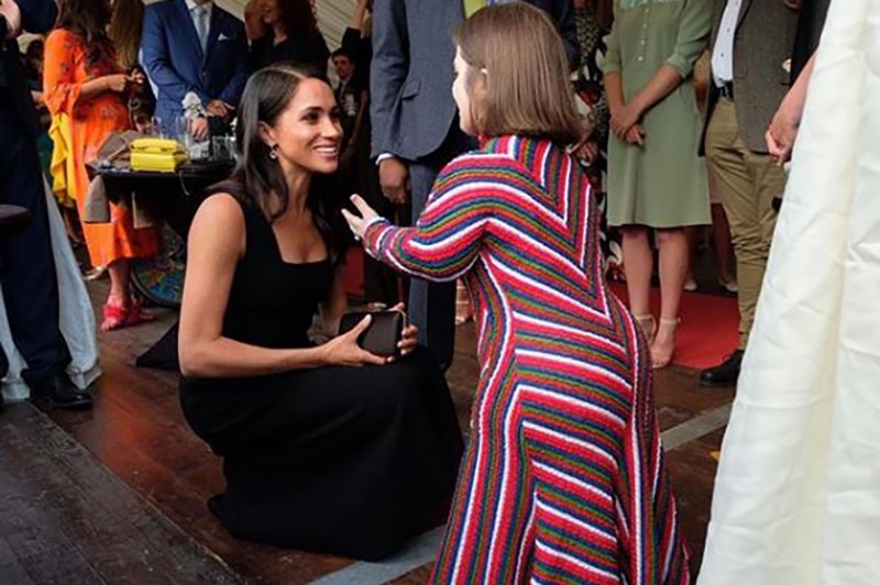 Sinead Burke with Meghan Markle, who is crouched down to greet her.