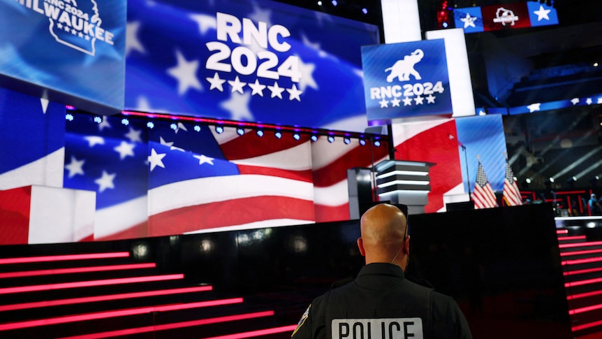A police officer stands in front of a stage lit up in red, white and blue.