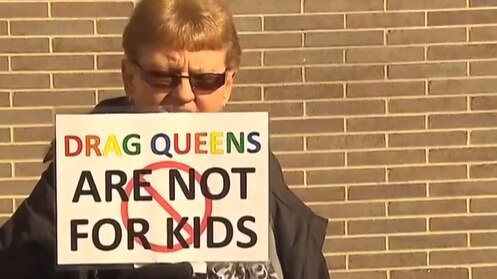 woman in dark sunglasses face slightly obscured by placard protesting about drag queens