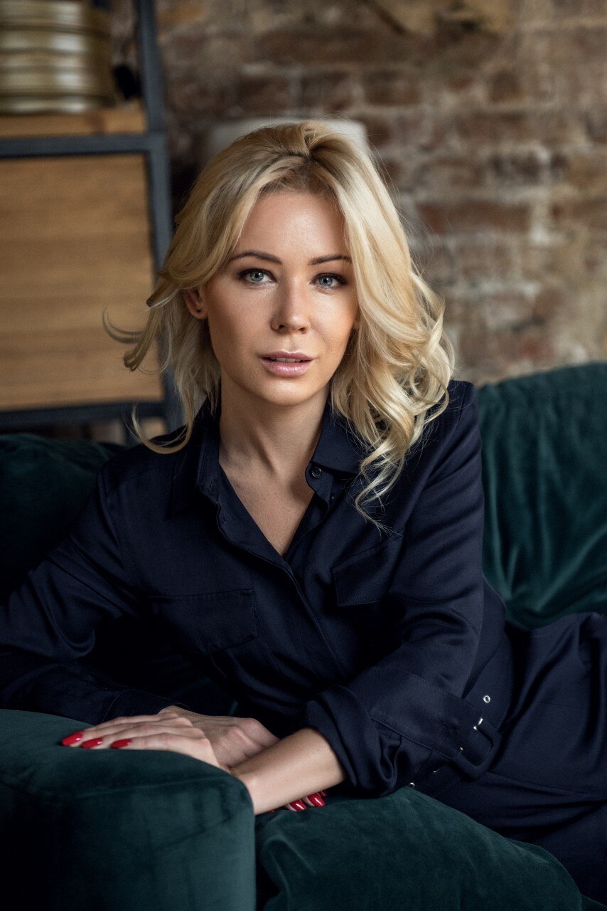 A woman sitting on a couch and looking at the camera with a  neutral expression.