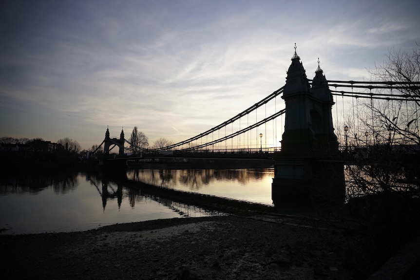 Hammersmith Bridge is reflected in the River Thames as the sun sets.